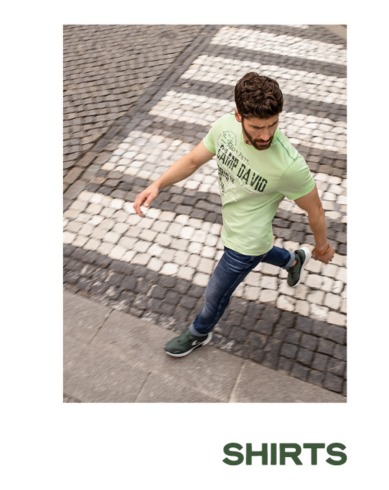 Model trägt ein grünes T-Shirt mit Jeans und läuft über die Straße.
