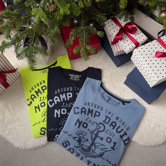T-Shirts und Geschenke liegen an einem Weihnachtsbaum