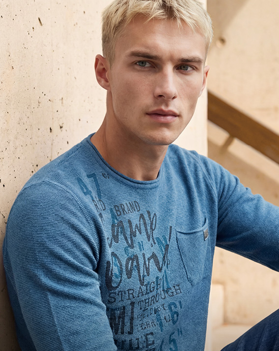 Model trägt blaue Jacke und hat Schnee im Gesicht